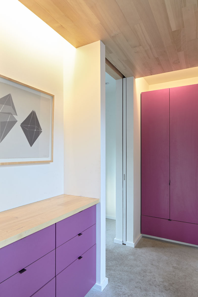 Stepping inside this modern house, you are hit with a burst of color with bright pink and purple cabinetry. Through a pocket door is the laundry, and hidden lighting in the ceiling creates ambient lighting in the entry. #BrightCabinets #InteriorDesign