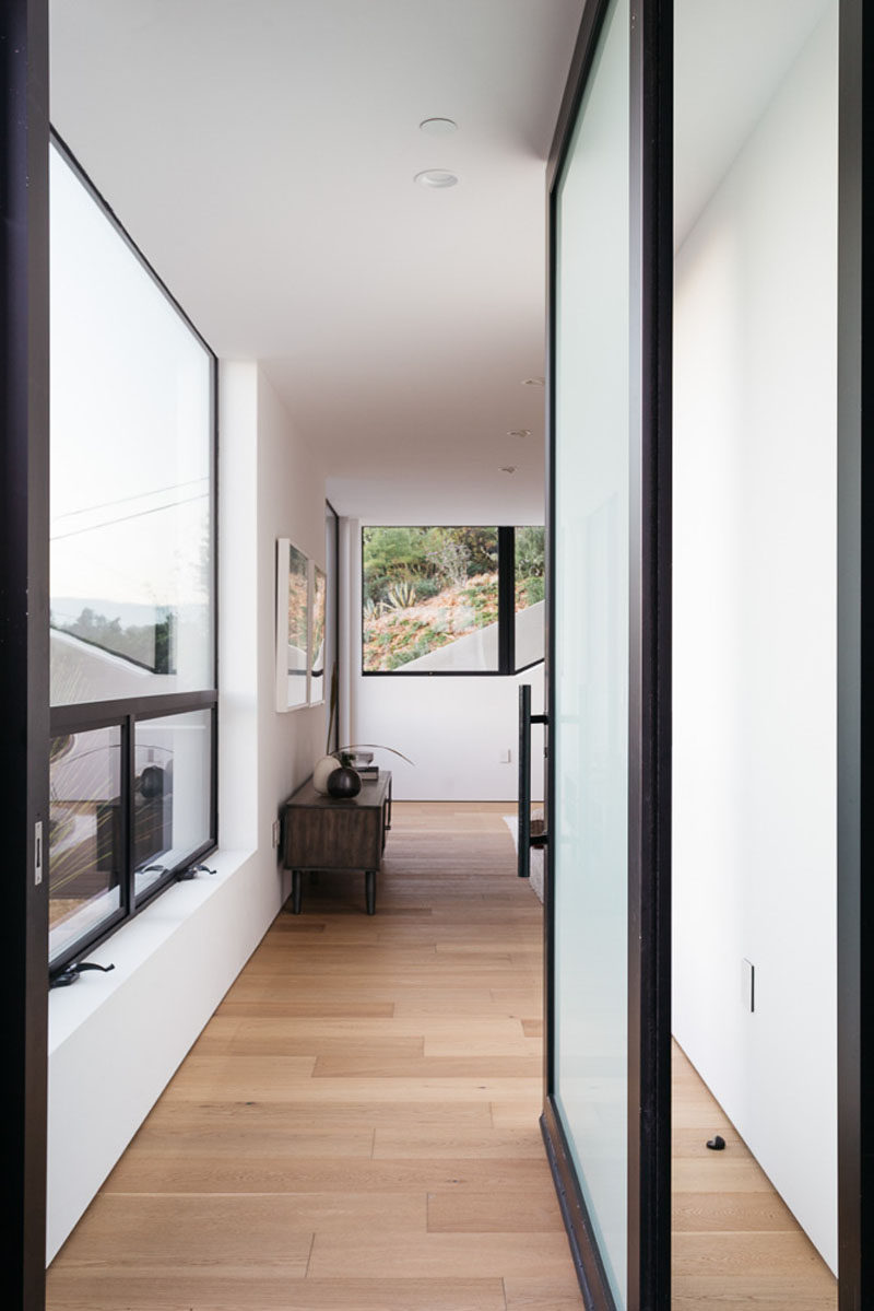 A semi-transparent front door and large windows allow natural light to fill the interior of this modern house. #FrontDoor #Windows #WoodFlooring