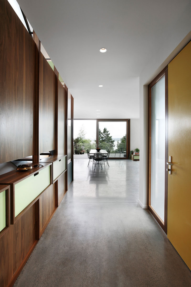 Stepping inside this modern house, there's a walnut accent wall with built-in shelving and a hallway leads to the main floor of the home. #YellowFrontDoor #Entryway