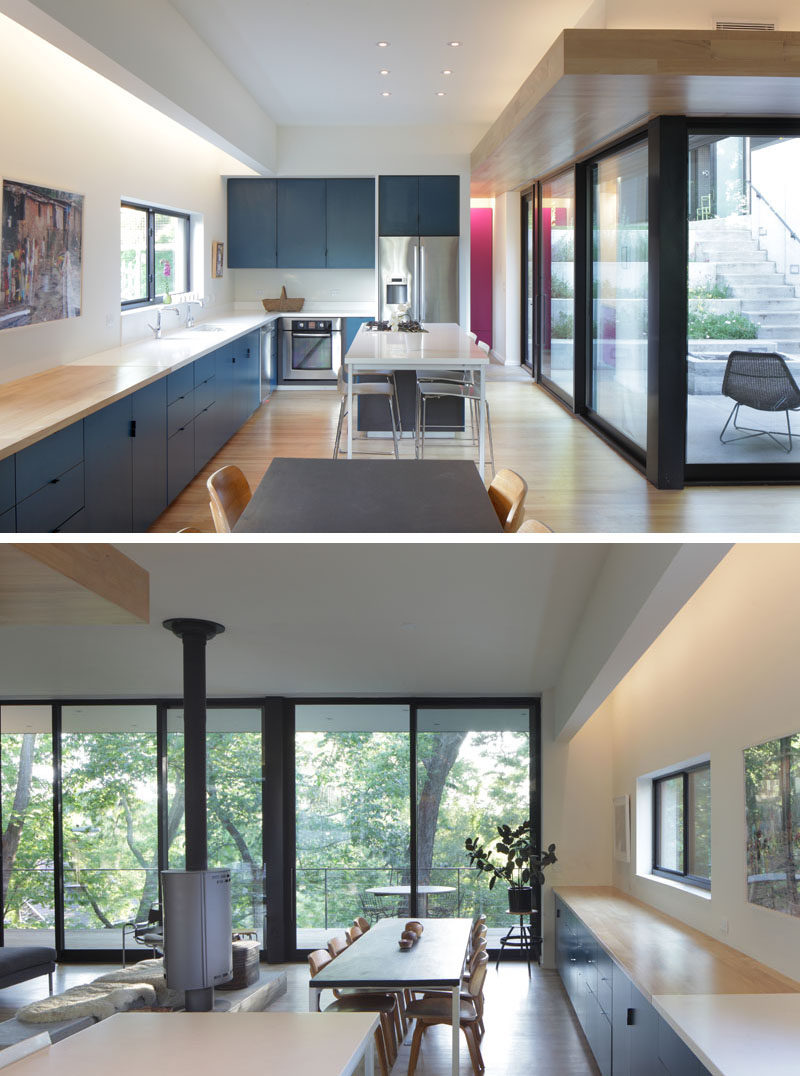 Navy blue cabinets that run the length of the wall have been topped with white counters in the kitchen, while wood counters help to define the dining area. #NavyBlueKitchen #KitchenDesign