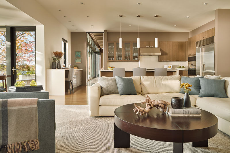 In this open floor plan, light wood cabinetry has been paired with white counters and stainless steel appliances for a contemporary kitchen. Next to the kitchen is a relaxed sitting area with a comfortable couch and armchair. #ContemporaryKitchen #SittingRoom