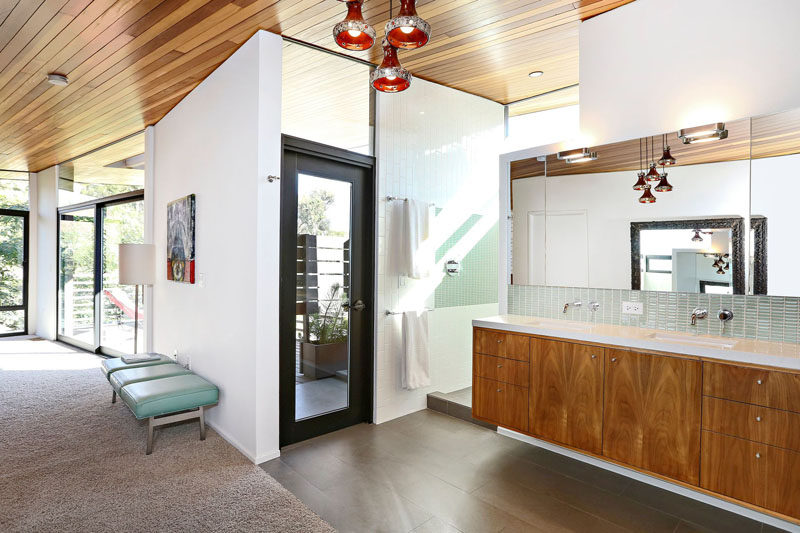 This modern master bedroom also has its own bathroom that's somewhat open to the rest of the room. A large double vanity sits next to the indoor shower, while through the black-framed glass door is an outdoor shower. #BathroomDesign #ModernBathroom