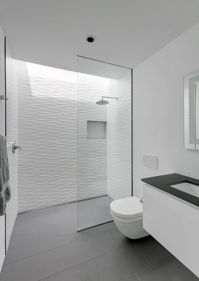 Grey floor tiles have been paired with textured white tiles to create a contemporary bathroom, while a skylight located above the shower adds a touch of natural light to the space. #ModernBathroom #WhiteAndGreyBathroom #BathroomDesign