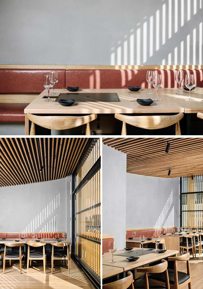 The interior of this modern Korean BBQ restaurant has soft grey walls and banquette seating with two banks of timber tables with integrated charcoal barbecues. Instead of having pendant lights hanging above the tables, the designers installed LED backlighting behind the banquettes. #RestaurantDesign #InteriorDesign