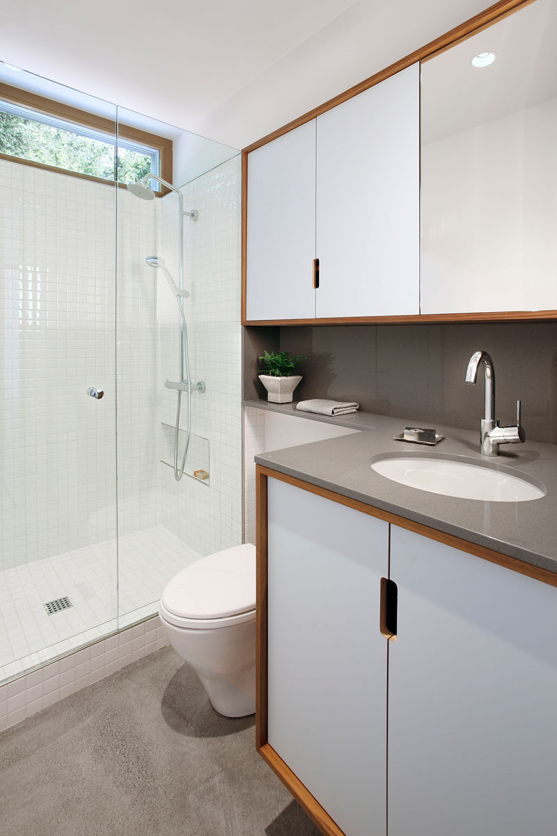 In this modern bathroom, a grey counter has been paired with white tiles, glass and wood frames to create a contemporary look. #ModernBathroom #BathroomDesign