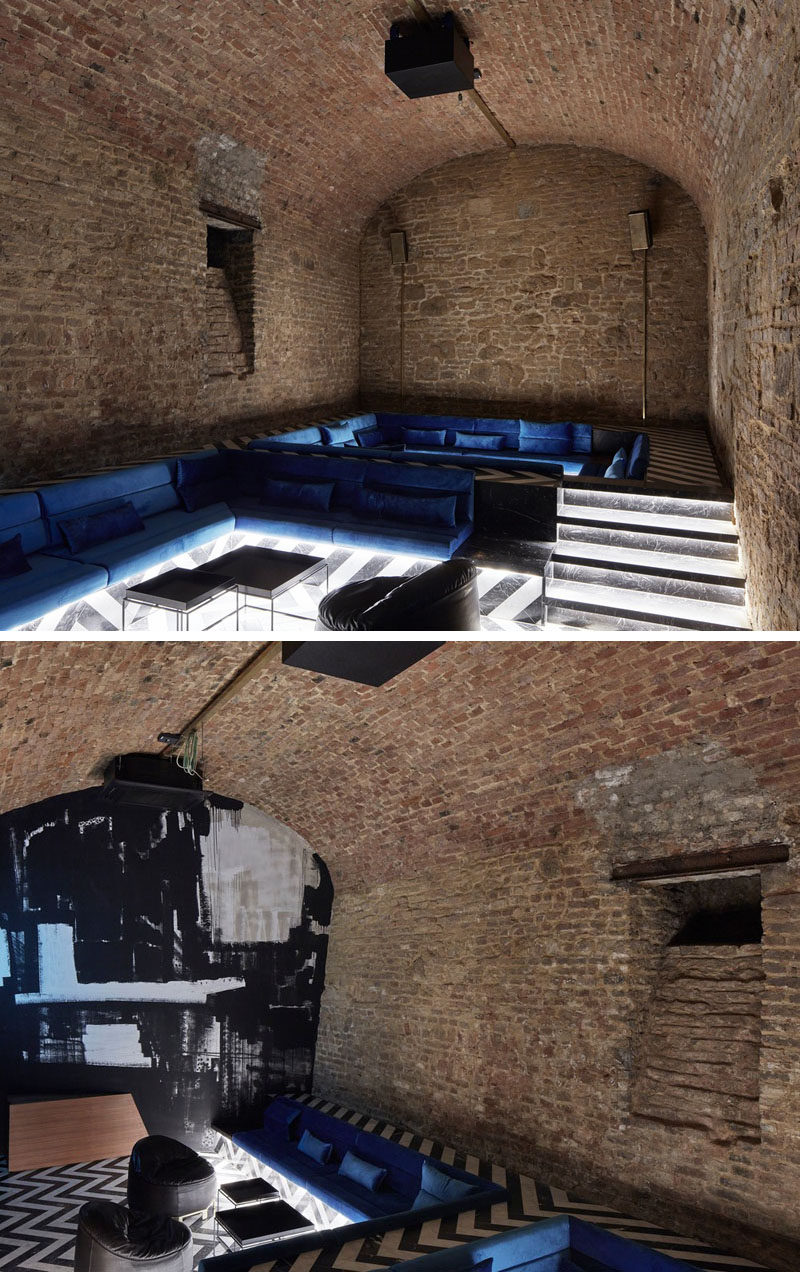 In this underground bar with stone alcoves, there's a raised floor that allows for a sunken lounge with blue couches and hidden lighting. #SunkenLounge #StoneAlcove #UndergroundBar