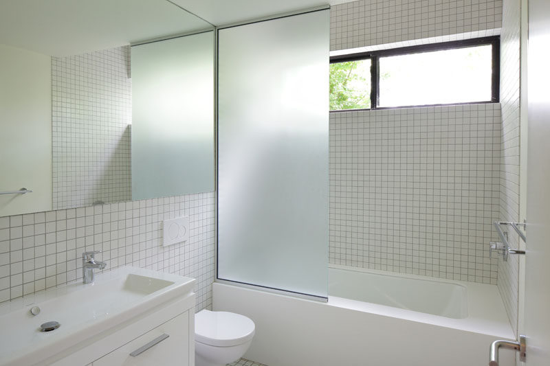 In this modern master bathroom, small square tiles cover the walls, while a frosted glass screen separates the bath/shower from the toilet and vanity. #MasterBathroom #BathroomDesign #ModernBathroom