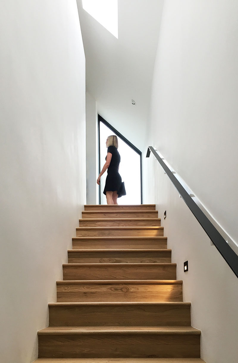 Connecting the garage and the upper floor of this modern house, is a light-filled stairwell with wooden stairs and a minimalist black handrail. #WoodStairs #StairDesign
