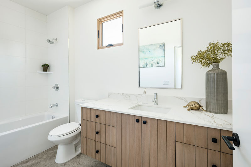 This modern bathroom has a small window with a wood frame that ties in with the wood cabinetry of the vanity. #ModernBathroom #WhiteAndWoodBathroom #BathroomDesign