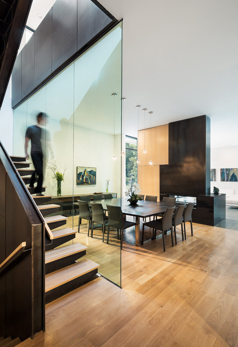 In this modern house, a large square dining area with a table big enough to seat nine people sits between the staircase and a fireplace. #DiningRoom #SquareDiningTable