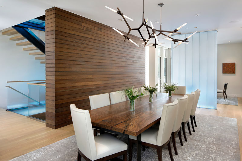 In this contemporary dining room sits beside a wood accent wall and a channel glass partition, while sculptural pendant lights add an artistic flair to the room. #DiningRoom #InteriorDesign