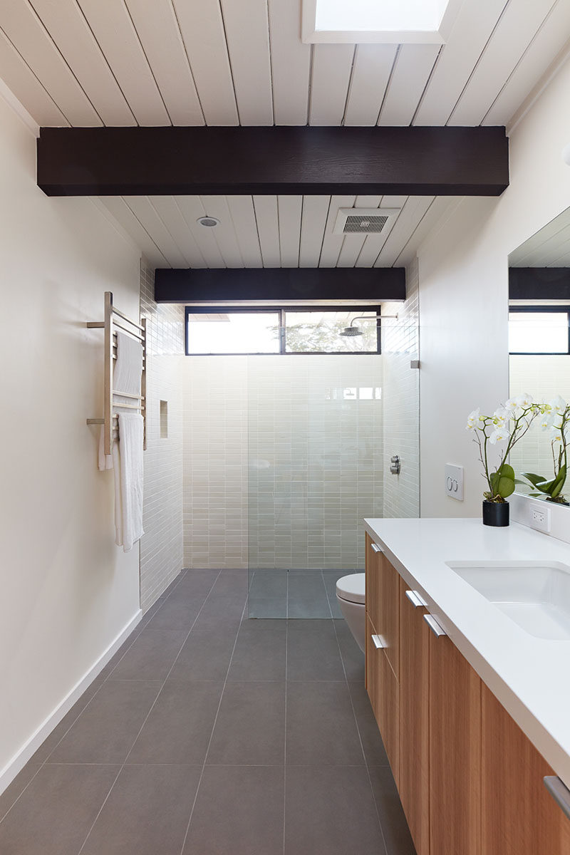 In this modern ensuite bathroom, large grey tiles cover the floor, while light colored tiles and a glass surround keep the shower bright. #ModernBathroom #BathroomDesign