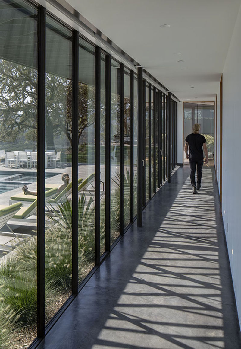 A long hallway with floor-to-ceiling windows connects the living areas of this modern house to the bedrooms. #ModernHallway #Windows