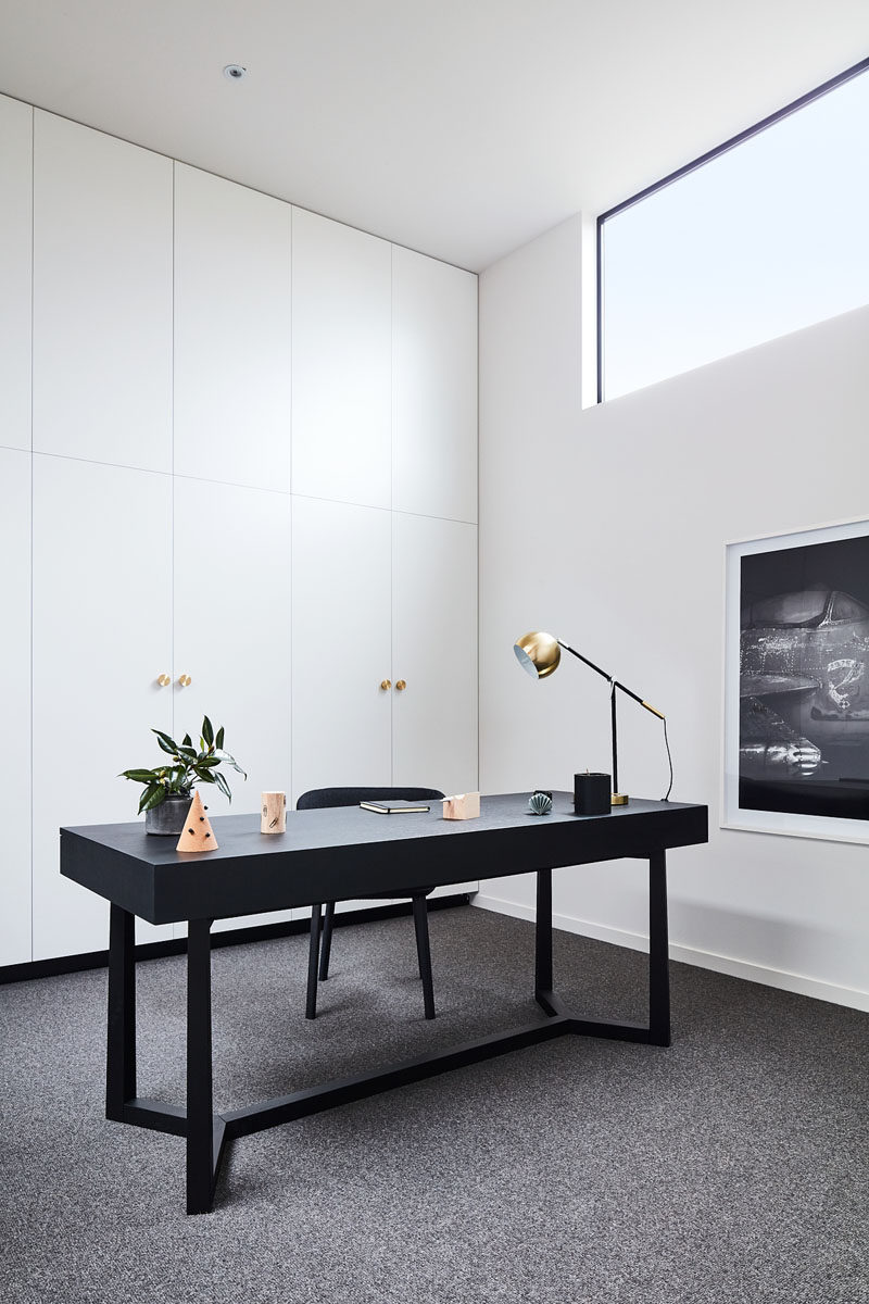 White minimalist cabinets line the wall in this home office, while the black desk complements the black window frames and artwork. #ModernHomeOffice #InteriorDesign