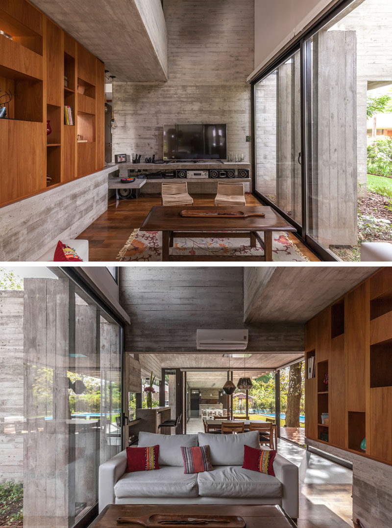 In this contemporary living room, a wood shelving unit runs along one wall, while large windows flood the room with light. #LivingRoom #Bookcase