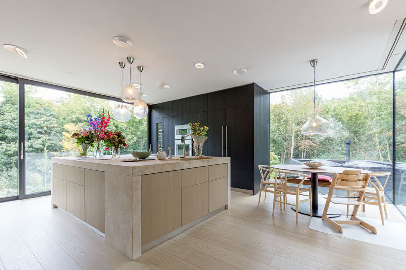 In this modern kitchen and dining room, a black box in the corner houses the ovens, fridge and storage cabinets, while the large island provides plenty of counter space. Next to the kitchen is a space dedicated to the dining table. #ModernKitchen #RoudDiningTable