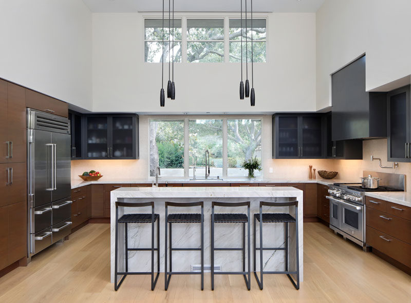 In this modern kitchen, the palette reflects the colors and materials used on the exterior of the house. Marble countertops are paired with stained base cabinets that match the exterior wood siding of the house, while a dark grey hood and upper cabinets match the exterior metal elements. #ModernKitchen #KitchenDesign