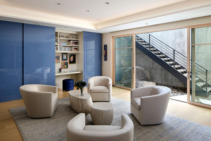 This contemporary sitting room has a hidden home office. In the adjacent light well, sculptural rock formations help create an element of interest, tying back to the outdoor landscape. #SittingRoom #InteriorDesign