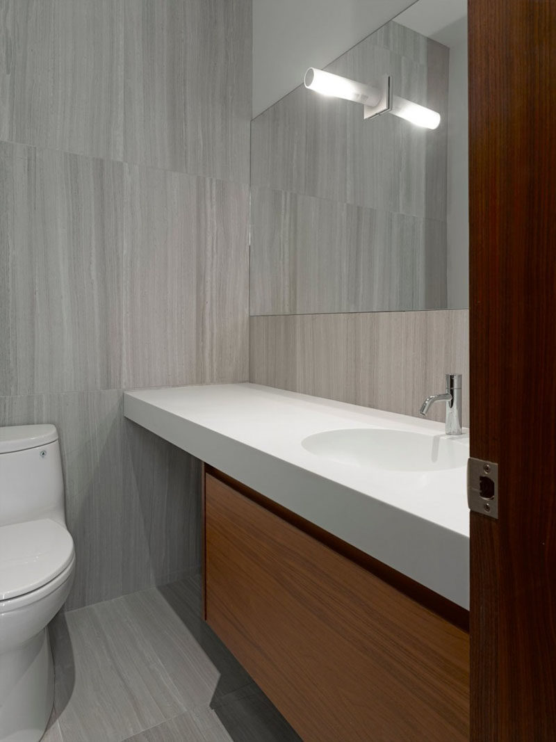 In this modern bathroom, large grey tiles, a white counter and wood vanity have been used to create a contemporary appearance. #ModernBathroom #GreyTiles #BathroomDesign