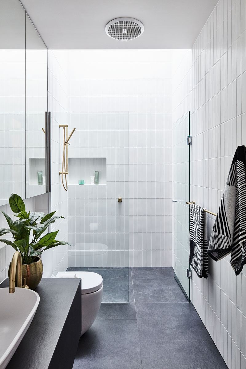 In this modern bathroom, floor-to-ceiling white tiles cover the walls, while a skylight adds natural light to the space. #ModernBathroom #BlackAndWhite #BathroomDesign