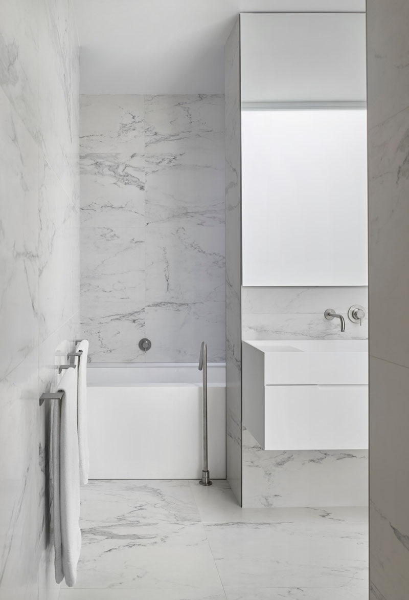 In this modern bathroom, grey stone tiles are combined with a minimalist white vanity and bathtub to create a contemporary look. #ModernBathroom #BathroomDesign