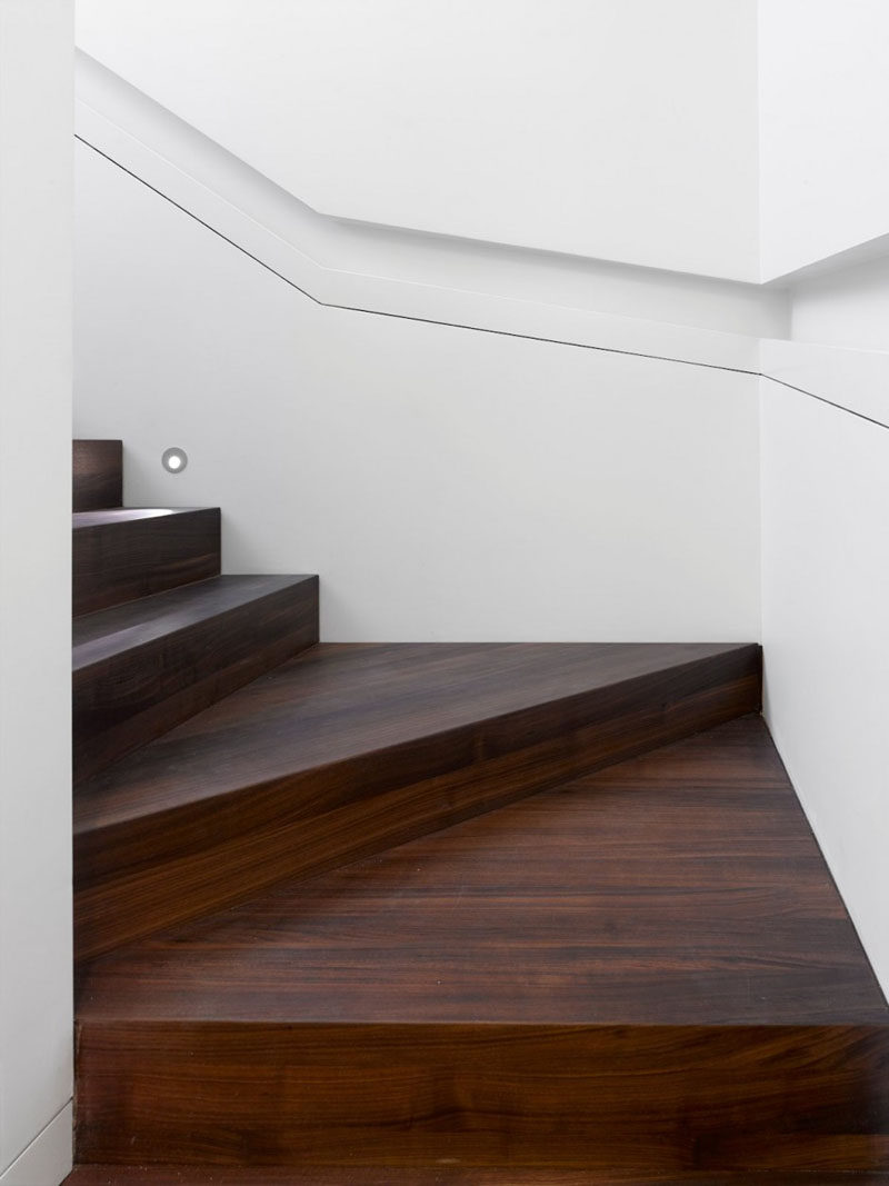 This modern house has wood stairs surrounded by white walls that lead up to the upper floor of the home. Built-in handrails create a simple and minimalist look for the stairwell. #WoodStairs #BuiltInHandrail