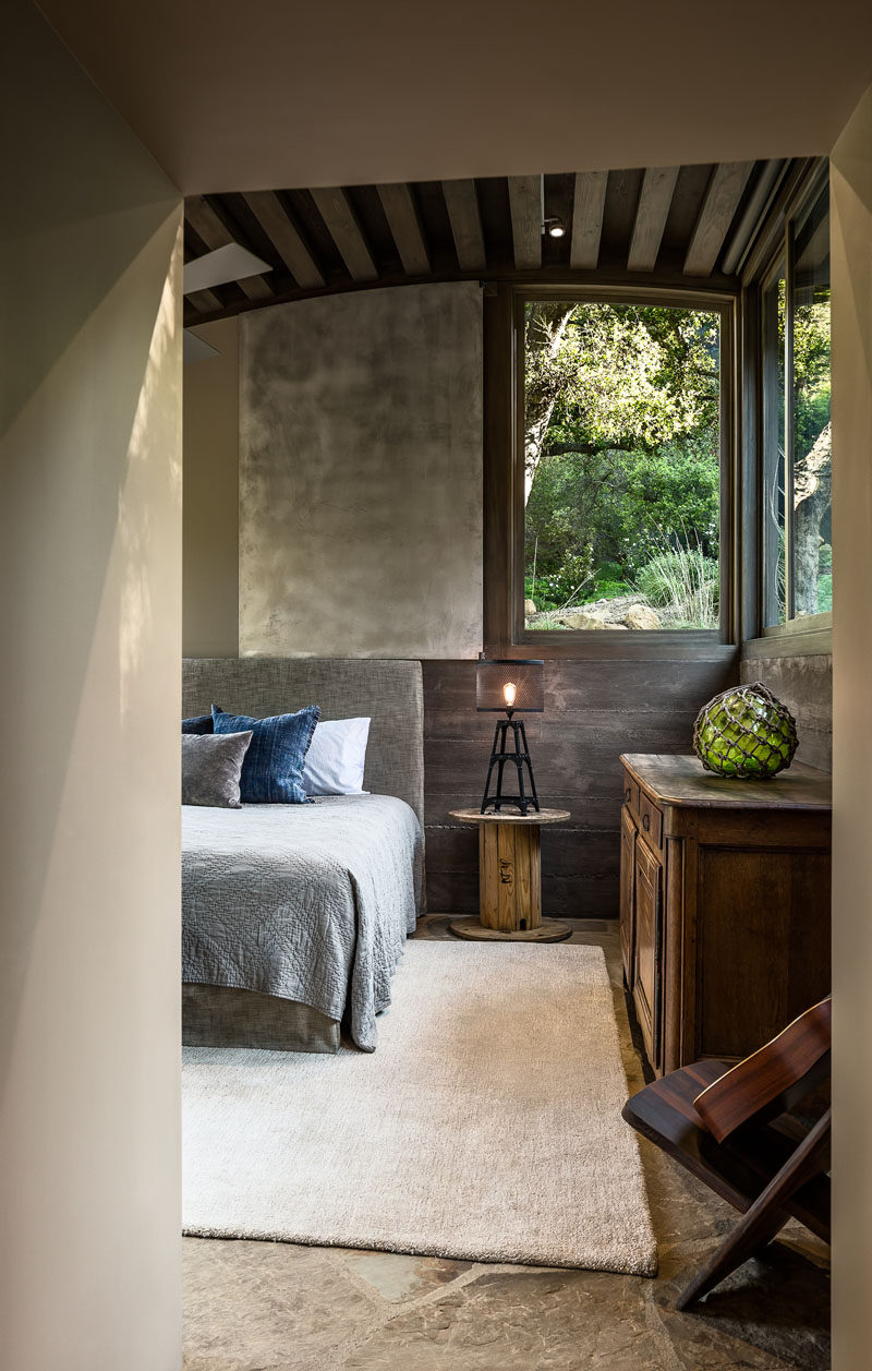 In this rustic modern guest bedroom, stained douglas fir beams have been used for the curved ceiling, while the walls are a combination of colored plaster and board-formed concrete. #GuestBedroom #CurvedCeiling #BoardFormedConcrete