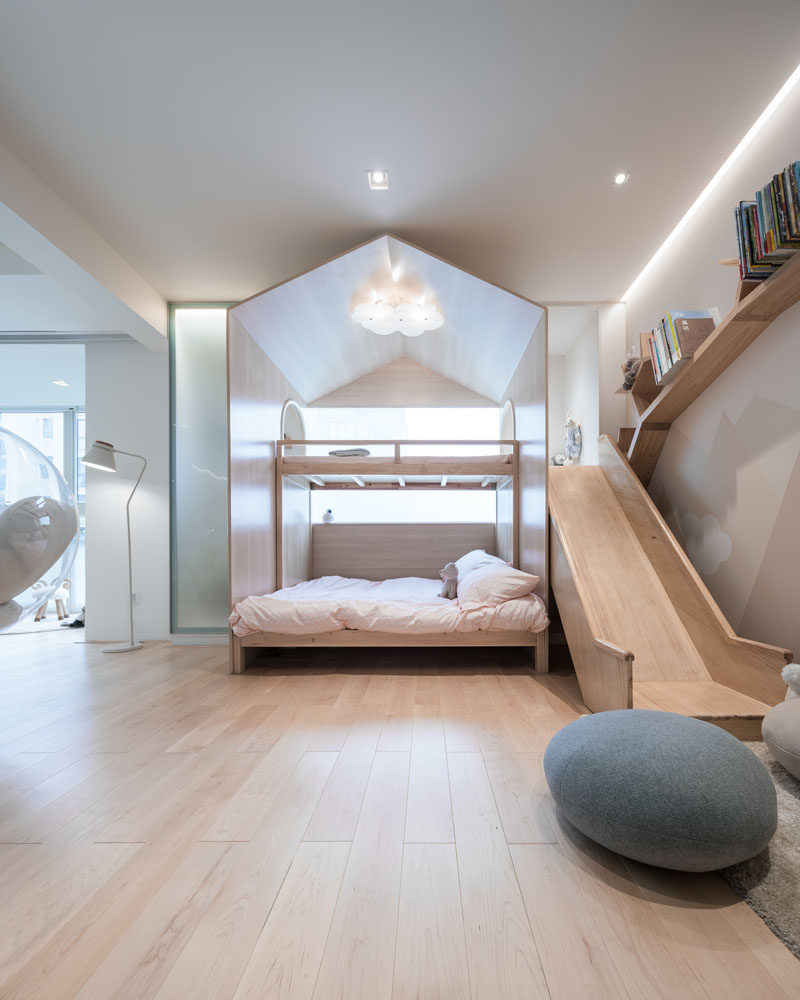 In this modern children's bedroom area, there's a bed built into the play structure with a slide, and on the wall next to the slide is a branch-like wood bookshelf. #KidsBedroom #KidsPlaySpace