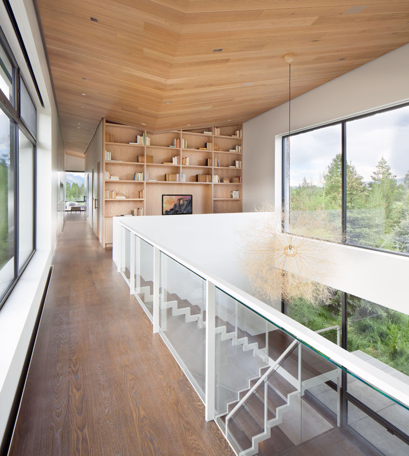 Stairs lead to the upper floor of this modern house, and a large double-height space allows the natural light from the windows to flood the interior. At the top of the stairs there's a small library area with a built-in bookcase. #Stairs #Shelving #WoodCeiling