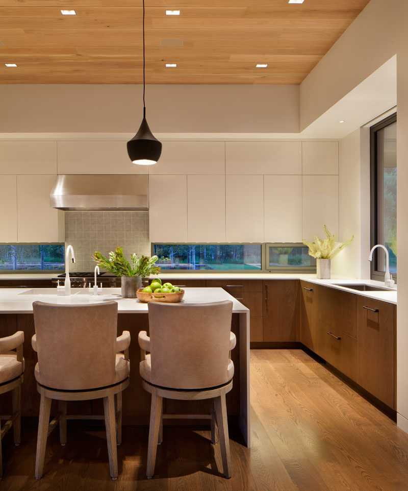 In this kitchen, minimalist white cabinets, a white island and white countertops have been combined with lower wood cabinets to create a contemporary look. #Kitchen #ContemporaryKitchen