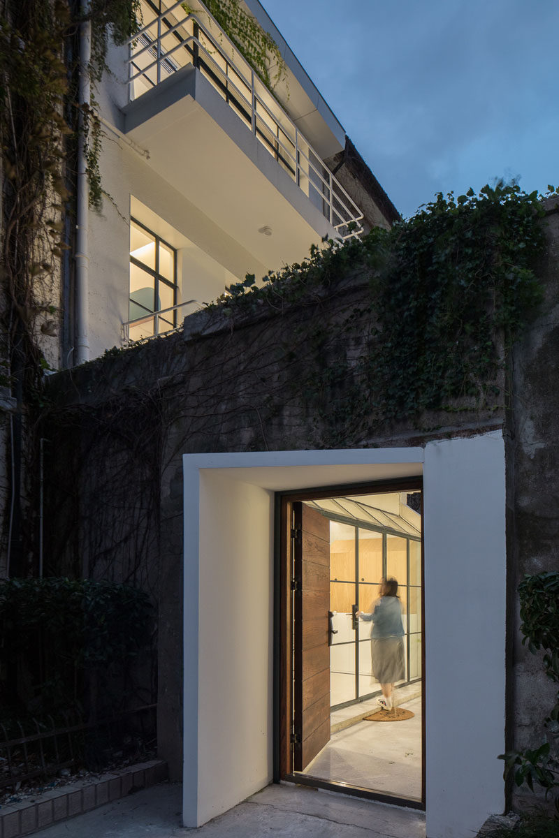 The white entryway and wood door of this modern house stand out against its concrete and vine surroundings. #ModernHouseEntry #FrontDoor