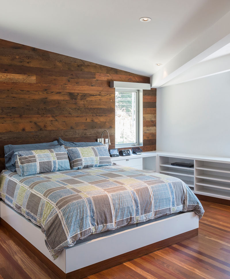 In this contemporary master bedroom, a wood accent wall and wood flooring add a natural touch to the all wall white room. #MasterBedroom #WoodAccentWall