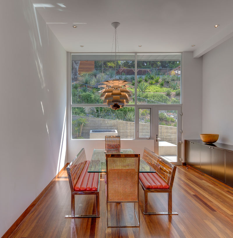 This contemporary dining room is furnished with a glass dining table and bench seating, while large windows provide a view of the landscaped backyard. #DiningRoom #Windows