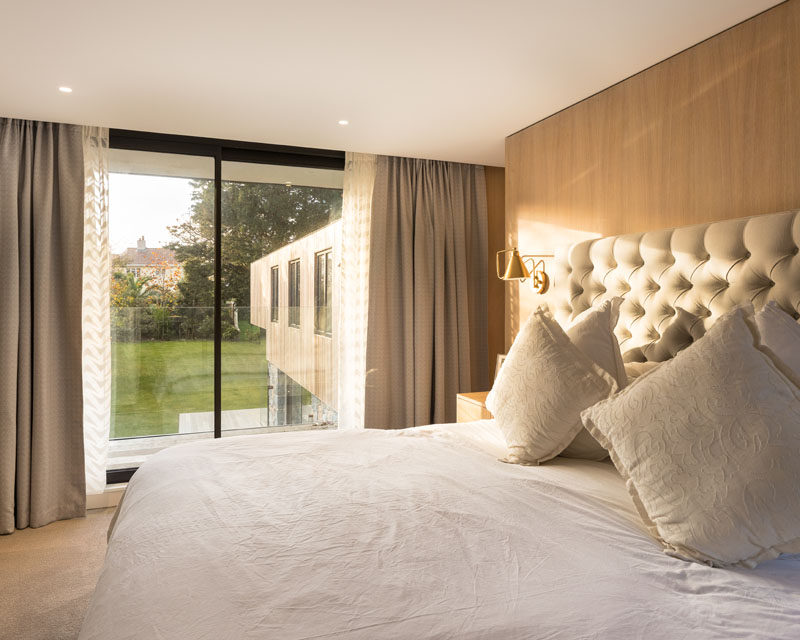 In this contemporary master bathroom there's a wood accent wall behind the bed, and a sliding glass door opens up to a small balcony with views of the garden. #MasterBedroom #BedroomDesign