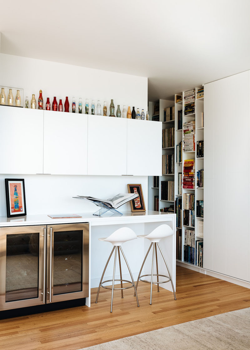 This modern bar area has a couple of drink fridges and cabinets for storage. The home owners Coca-Cola bottle collection sits on top of the cabinets and stands out against the white walls. #WhiteCabinetry #Bar