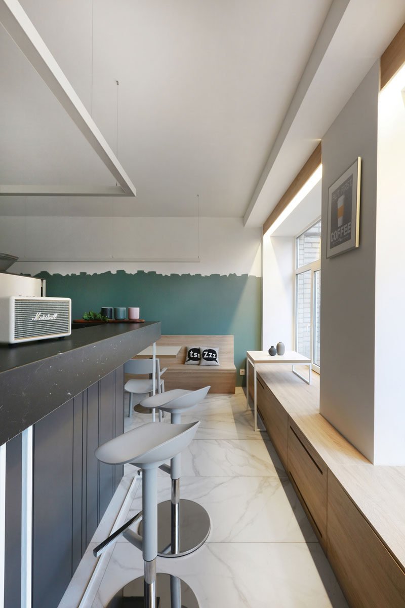 Running along the back wall of this modern coffee shop and underneath the windows is a custom window sill that also acts as a wood bench to creates additional seating, and allows people to gaze out of the window. #WindowSill #WindowSeat #CoffeeShop