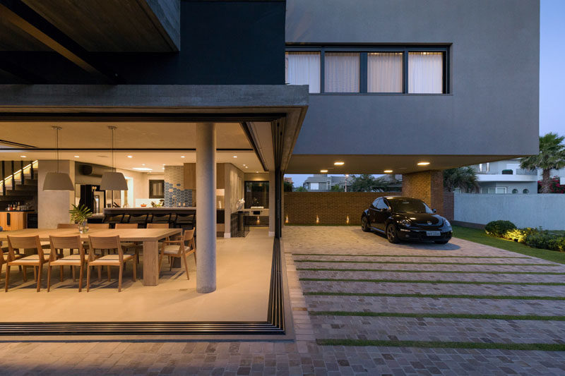 Sliding glass walls open up the dining room and interior of this modern house the driveway and carport. #GlassWalls #Carport #Driveway