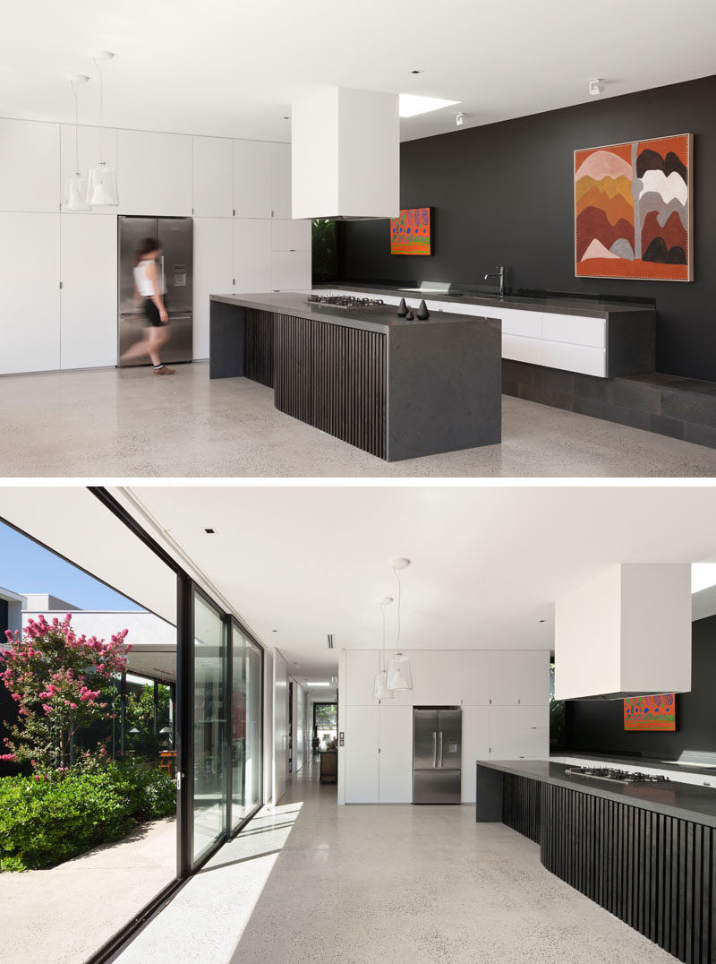 In this modern kitchen, a wall of white cabinets blend into the wall and surround the fridge, while an island provides additional counter space. #ModernKitchen #KitchenDesign