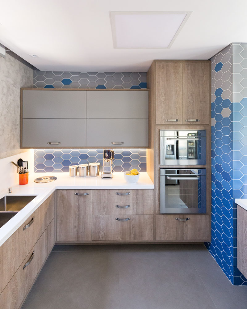 In this modern kitchen, hexagonal blue and light grey tiles cover the walls, while light wood and grey cabinets are combined with a white countertop to keep tings bright. #ModernKitchen #HexagonalTiles