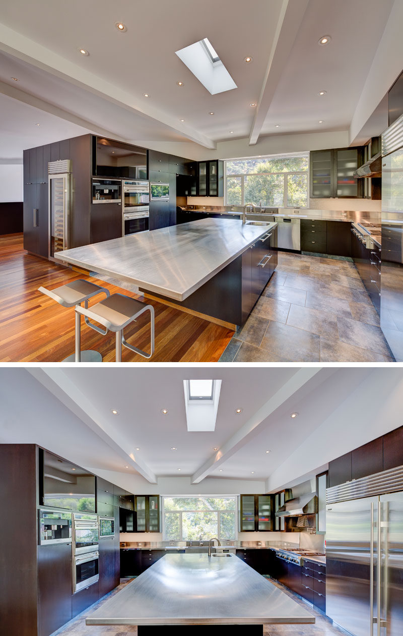 In this modern and expansive kitchen, there's a large island centrally located in the U-shaped kitchen, while windows above the sink and a skylight add natural light to the space. #KitchenDesign #KitchenIsland