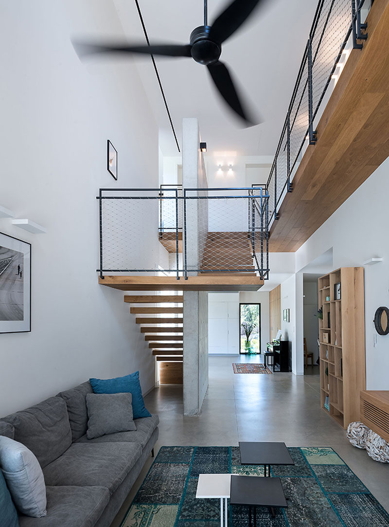 This modern living room with a double-height ceiling, has blue cushions on the couch that match the blues in the rug. #LivingRoom