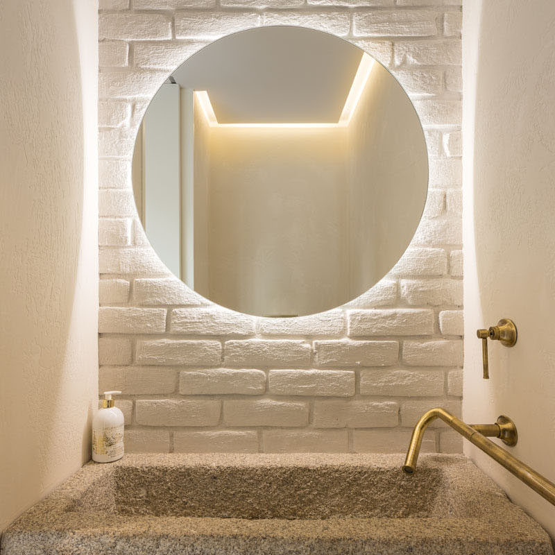 This small powder room has has a reclaimed granite trough as the sink and a backlit mirror. #PowderRoom #BacklitMirror #GraniteSink