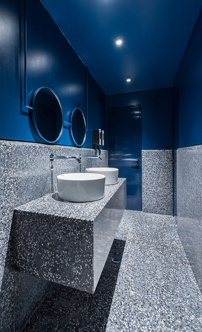 In this modern bathroom, a dark  blue paint has been used to create a drama appearance that ties into the blues used throughout the rest of the restaurant. #RestaurantBathroom #BathroomDesign