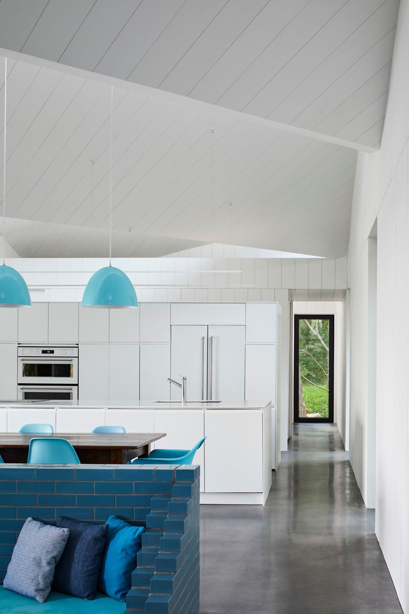 Stepping inside this modern house, the interior is fun and welcoming, with bright white walls and ceilings, a polished concrete floor with turquoise furnishings and design elements. #WhiteInterior #BlueFurniture #WhiteAndBlueInterior