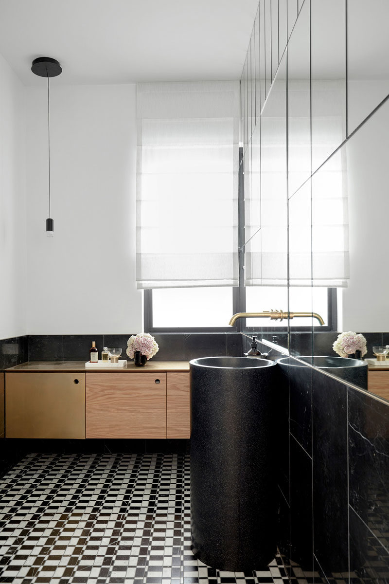 In this contemporary bathroom, the upper part of one wall is covered in mirrors, making the sunlight from the window reflect around the mostly white and black interior. #Bathroom #BlackAndWhite