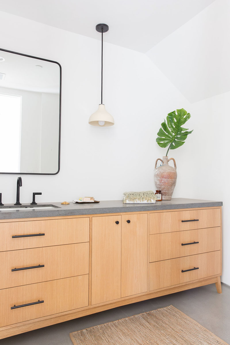 In this modern bathroom, there's a large wood vanity with a concrete countertop and black hardware. #BathroomDesign #WoodAndConcrete