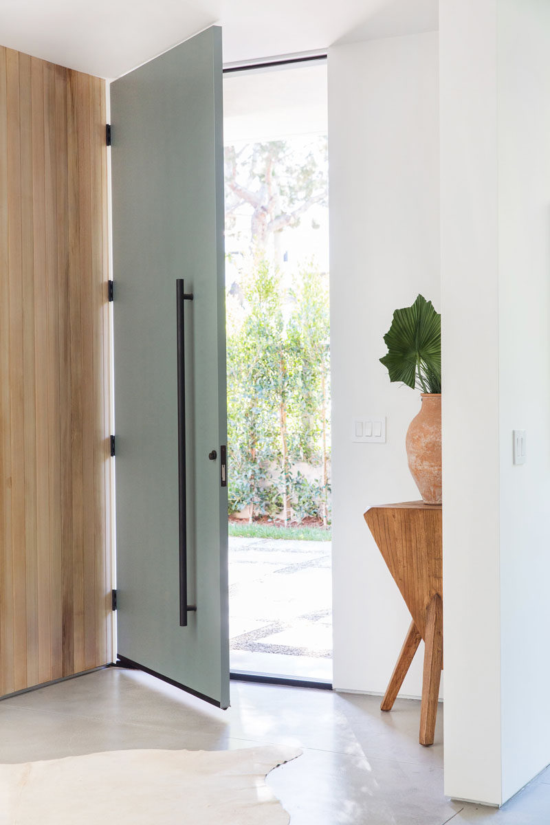 A tall, full-height grey front door with matte black hardware welcomes visitors to this mid-century inspired home. #FrontDoor