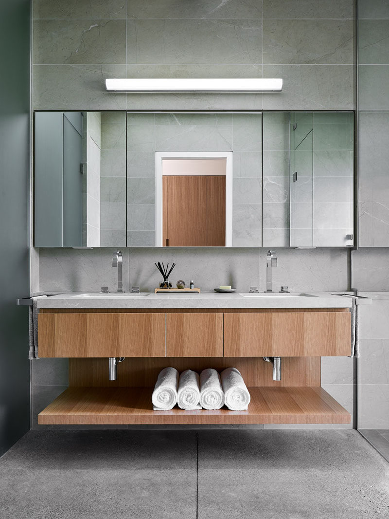 In this modern master bathroom, a double sink vanity with open shelving separates the shower from the toilet. #Vanity #MasterBathroom #BathroomDesign