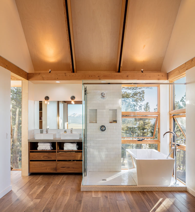 This modern and open bathroom has a glass-enclosed shower that sits next to a freestanding bathtub with views of the trees. #Bathroom #ModernBathroom #GlassEnclosedShower