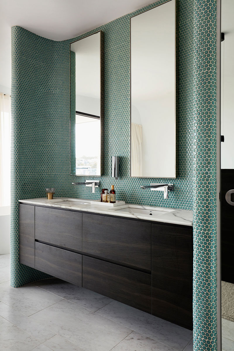 In this modern bathroom, green penny tiles have been used to create an accent wall behind the tall mirrors and vanity. #PennyTiles #TileAccent #Bathroom